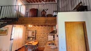 A rustic kitchen with a stone wall, wooden beams, and a dining area with a table and chairs. - Olivaia-beautiful loft apartament with view (Reggello)