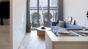 A modern living room with a sofa, a coffee table, and a dining area with a glass of wine and plates. - BaseLIVING Wending Serviced Apartment (Shanghai)