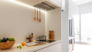 A modern kitchen with white cabinets, a wooden bowl of fruit, a cutting board, and a pot on the counter. - BaseLIVING Wending Serviced Apartment (Shanghai)
