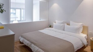 A modern bedroom with a large bed, a bedside table, and a window providing natural light. - BaseLIVING Wending Serviced Apartment (Shanghai)