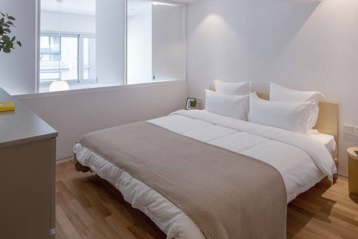 A modern bedroom with a large bed, a bedside table, and a window providing natural light.