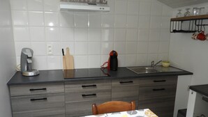 A modern kitchen with a dining area. It includes a coffee maker, a toaster, and a kettle on the counter. There is a sink and a wooden cutting board. The table is set with a plate, a fork, and a knife. - Independent studio on the 1st floor less than 1 kilometer from the Château de Lavaux (Rochefort)