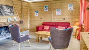 A cozy room with wooden walls, a red sofa, two armchairs, a wooden table, and a fireplace.