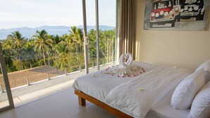 Camera da letto con un letto grande, vista su palme e montagne, e un quadro appeso al muro.