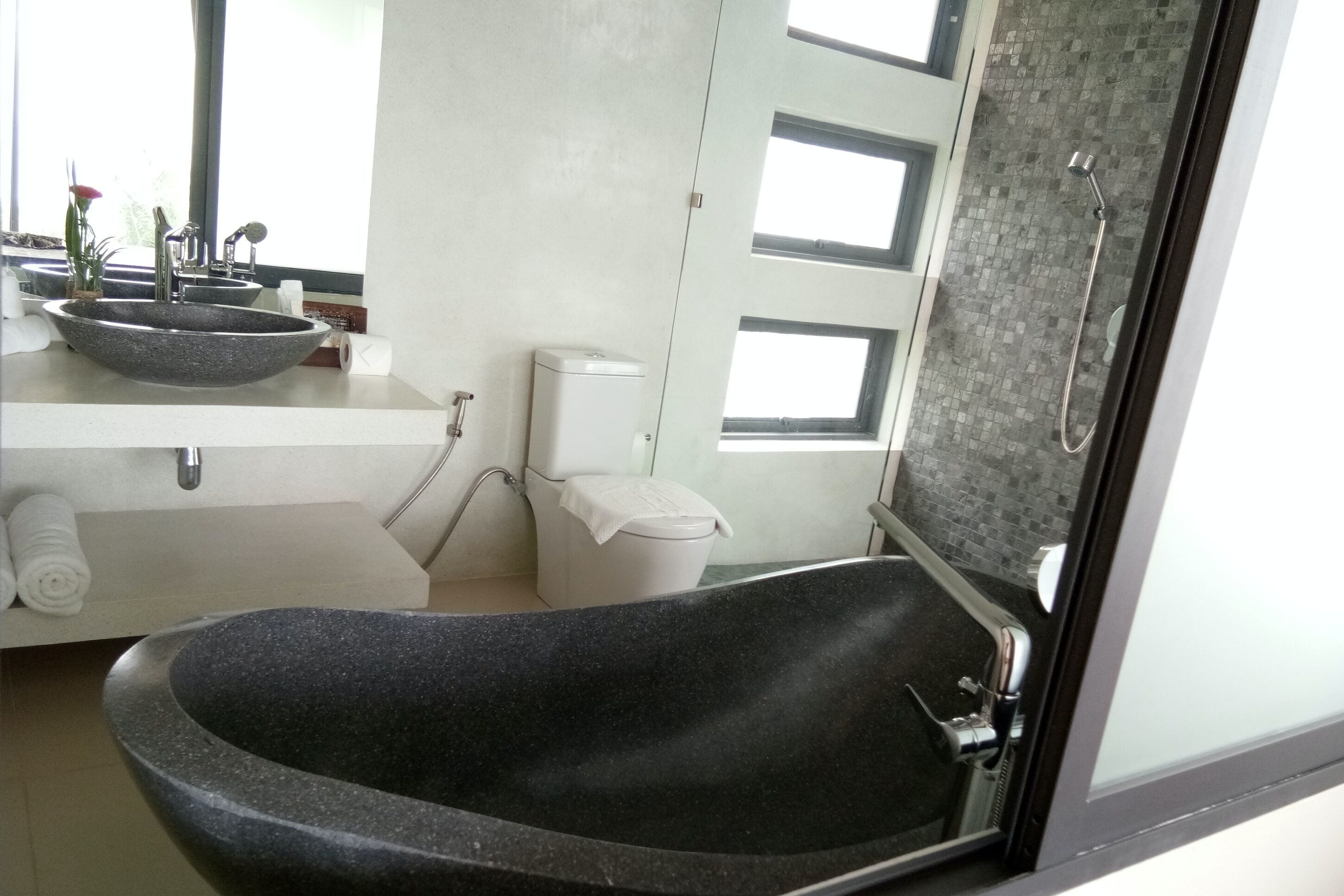 A bathroom with a black freestanding bathtub, a white sink with a granite countertop, and a toilet.