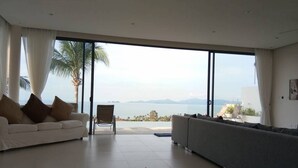 Un ampio soggiorno con una grande porta scorrevole in vetro che dà su un balcone con vista sul mare.