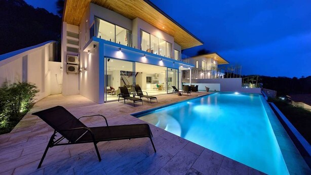 Una casa moderna con piscina, area salotto esterna e ampie finestre.