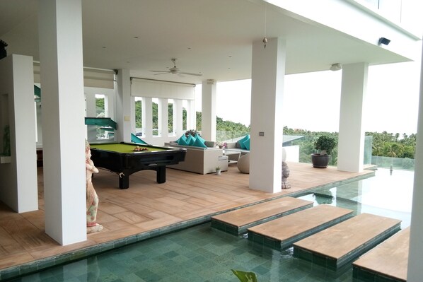 Un área de piscina con mesa de billar y asientos tipo sala de estar.