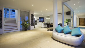A modern living room with a curved sofa, a staircase, and a kitchen in the background. - 6 Bedroom Luxury Sea View Villa Moonrise SDV079B-By Samui Dream Villas (Koh Samui)