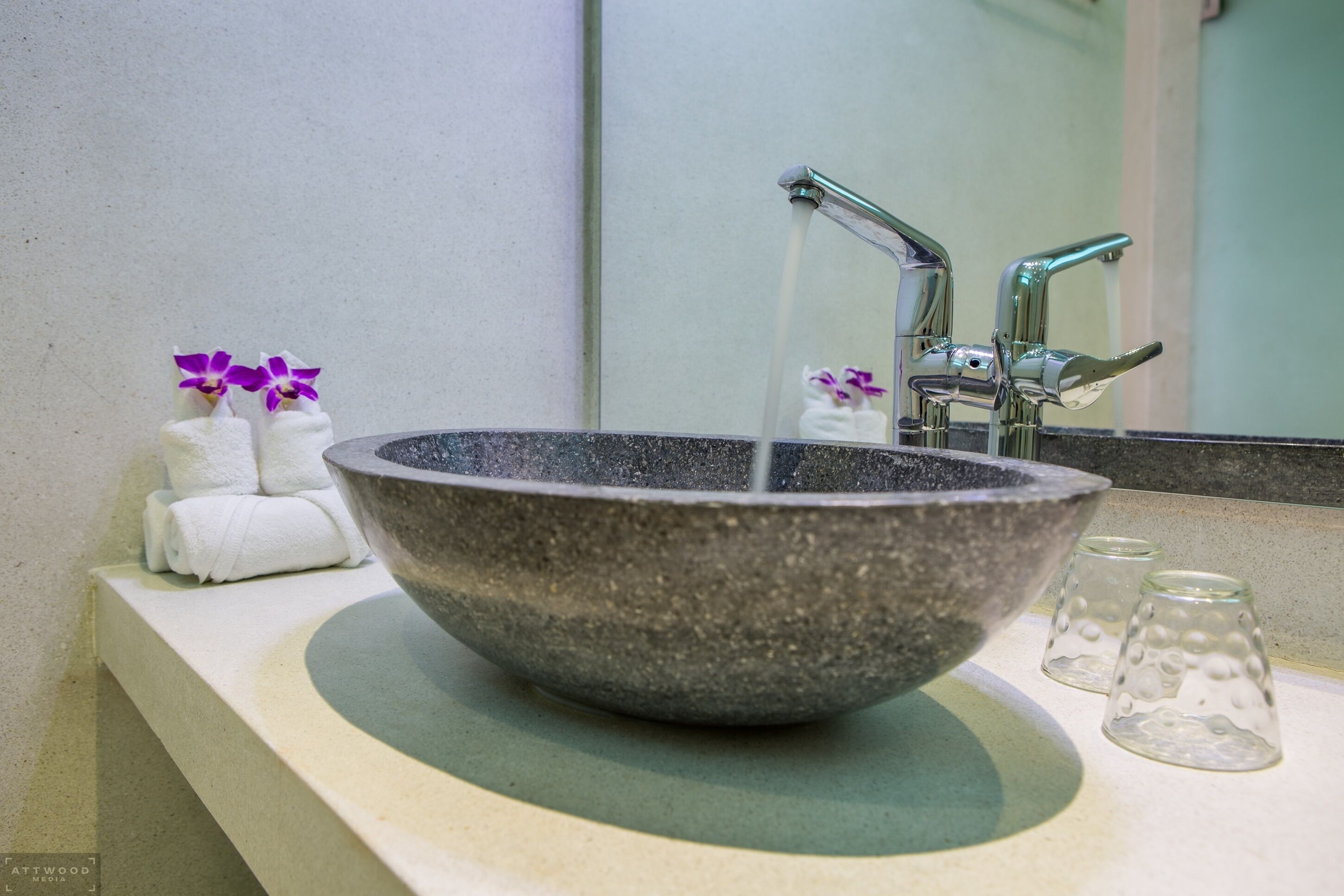A stone basin sink with a faucet, two towels, and two glass cups on a countertop.