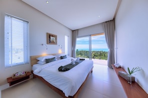 A modern hotel room with a large bed, a view of the ocean, and a balcony with a potted plant.