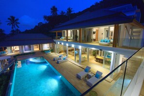 Una casa moderna de dos pisos con piscina, mobiliario exterior y ventanas amplias.