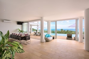 A spacious living area with a dining table set for a meal, a comfortable seating area with a view of the ocean, and large windows allowing natural light.