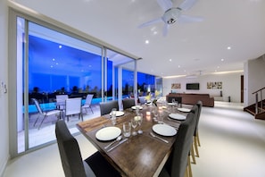 A modern dining area with a large table set for six, large windows, and a view of an outdoor pool area.