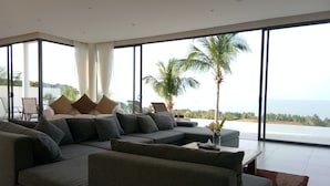 Een moderne woonkamer met een grote hoekbank, een salontafel en uitzicht op de oceaan door middel van ramen van vloer tot plafond.