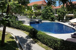 Une piscine entourée de verdure, un bâtiment avec un toit rouge et un chemin pavé.
