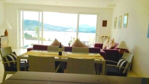 A dining area with a table and chairs, a sofa with cushions, and a view of a body of water and hills. - 6 Bedroom Sunset Sea Views Twin Apartments SDV120/097-By Samui Dream Villas (Koh Samui)