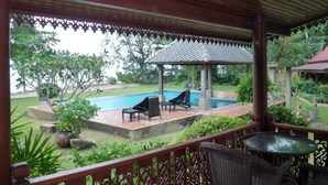 Un espacio exterior techado con piscina, sillones de descanso y un pabellón.