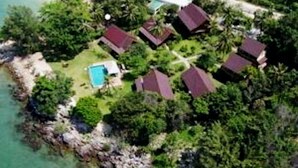 Vista aérea de una propiedad costera con varias casas, una piscina y abundante vegetación.