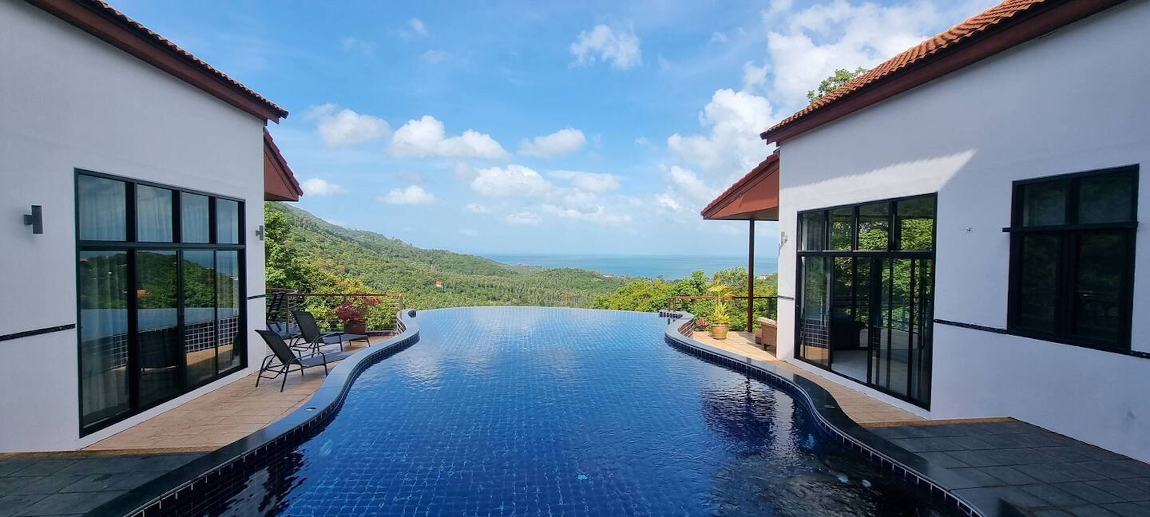 A modern infinity pool with a clear view of the ocean and hills.