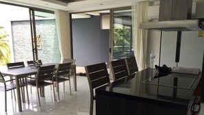 Un'area pranzo moderna con un tavolo in vetro e sedie, un laptop sul tavolo e vista sul mare attraverso ampie finestre.