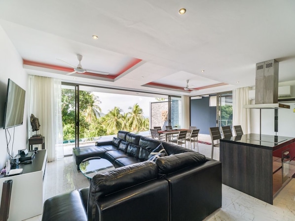 A modern living room with a black leather sofa, a dining area, and a kitchen with a glass island.