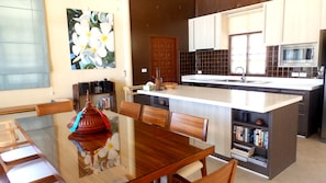 A modern kitchen with a central island, wooden chairs, a dining table, and a bookshelf. - 4 Bedroom Beach Front Villa Sea Breeze SDV229B-By Samui Dream Villas (Koh Samui)
