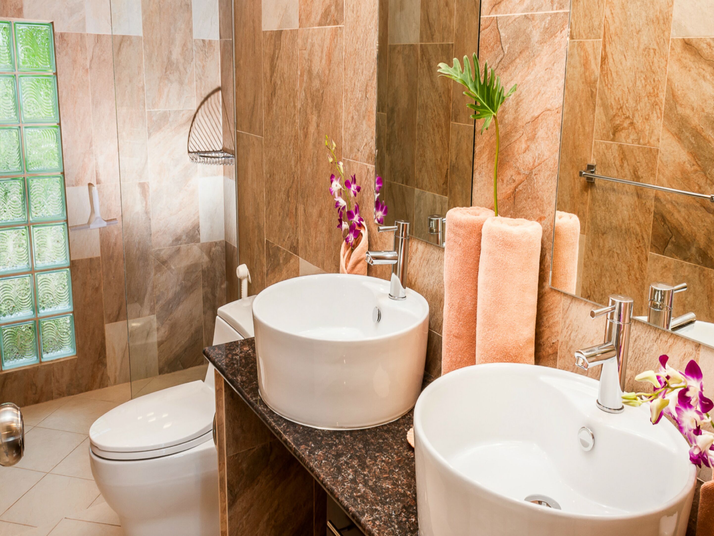 A bathroom with two sinks, a toilet, a glass shower enclosure, and a large mirror.