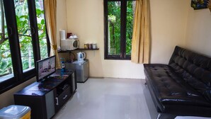A compact living space with a black leather sofa, a small kitchenette with a microwave and kettle, and a window with curtains. - 1 Bedroom Beach Bungalow Koh Phangan SDV235-By Samui Dream Villas (Ko Pha-ngan)