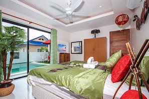 A bedroom with a bed, a ceiling fan, a wooden wardrobe, a television, and a view of a swimming pool.