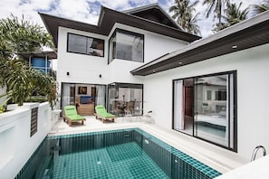 Una casa moderna de dos pisos con piscina, ventanas amplias y un balcón.