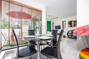 A dining area with a glass table and chairs, a green door, and a painting of an elephant.