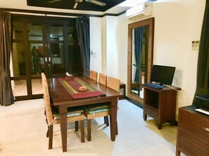 A dining area with a wooden table, wicker chairs, a TV on a stand, and a sliding glass door leading to a balcony.