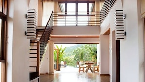 A spacious interior with a high ceiling, a wooden staircase, and a view of a lush garden through an open doorway. - 6 Bedroom Sea View Villas Kai Muk Mussourie (Koh Samui)
