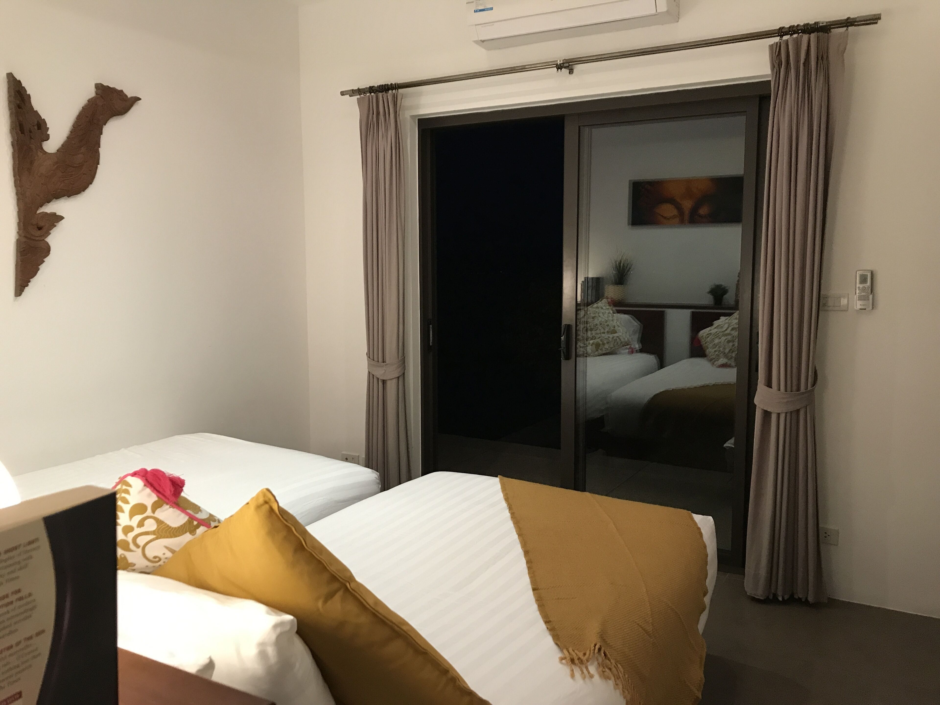 A hotel room with two beds, a sliding door to a balcony, and a wall-mounted air conditioning unit.