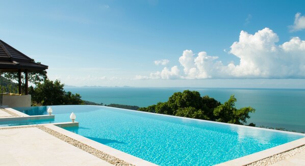 Ein klarer, blauer Infinity-Pool mit Blick auf das Meer und die entfernten Berge.