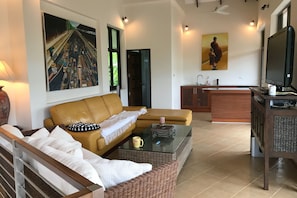 Un salon avec un canapé, une table basse et un téléviseur. Il y a un tableau au mur et une fenêtre donnant sur un beau paysage.