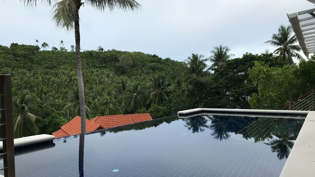 A clear view of a swimming pool with a tiled floor, surrounded by lush greenery and palm trees. - 3 Bedroom Sea View Villa Santi SDV228-By Samui Dream Villas (Koh Samui)