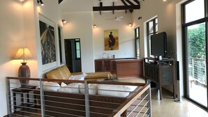 A spacious living area with a high ceiling, a sofa set, a television, and large windows offering a view of greenery outside. - 3 Bedroom Sea View Villa Santi SDV228-By Samui Dream Villas (Koh Samui)