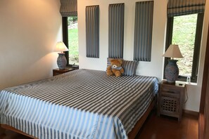 Een slaapkamer met een groot bed, gestreepte beddengoed, een teddybeer, twee bedlampen en een raam met gordijnen.