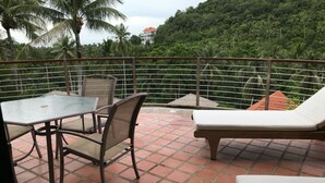 A terrace with a table and chairs, a lounge chair, and a view of a lush green hill with palm trees. - 3 Bedroom Sea View Villa Santi SDV228-By Samui Dream Villas (Koh Samui)