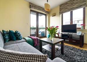 A living room with a sofa, a coffee table, a TV, and a view of the outside. - P&O Apartments Wilanow 7 (Warsaw)