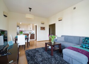 A modern living room with a grey sofa, a coffee table, and a dining area with a table and chairs. - P&O Apartments Wilanow 7 (Warsaw)