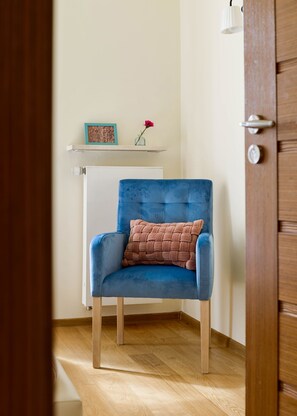 A room with a blue armchair, a wooden door, a white radiator, and a shelf with a picture and a vase. - P&O Apartments Wilanow 7 (Warsaw)