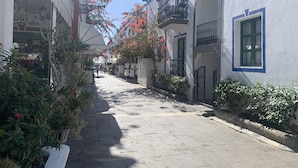 Uma rua estreita ladeada por edifícios, alguns com sacadas e caixas de flores, sob céu claro.