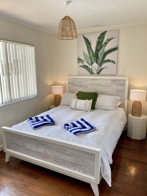 A neatly made bed with white bedding and blue striped towels, a woven pendant light, a framed botanical print, and two bedside lamps. - Location Is Everything plus WiFi (Jurien Bay)