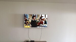 Un televisor montado en la pared con un mueble bajo de madera.