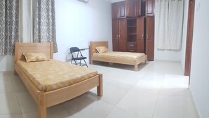 Una habitación con dos camas de madera, una silla, un armario y una mesita.