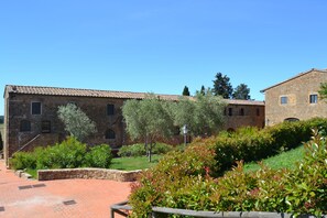 A courtyard with stone buildings, a paved walkway, and green shrubbery.