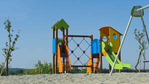 Eine Spielplatzanlage mit mehreren Rutschen und Kletterbereichen, umgeben von Sand und vereinzelter Vegetation.